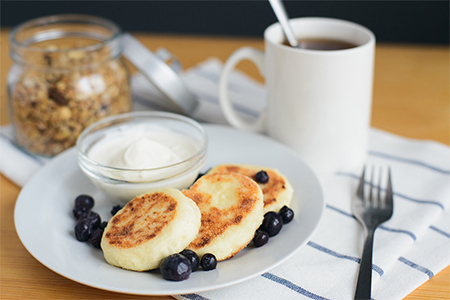 breakfast, circular syrniki, tvorozhniki or cheese cake with sour cream and hot drink on wooden tabl