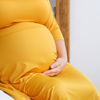 Pregnant woman in yellow dress sitting on bed and touching her belly