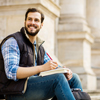 a student sitting on university stairs outside writing on paper