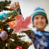 A young boy holding Christmas ornaments and placing them on the Christmas tree