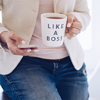 woman using mobile phone sitting on top of desk with a cup of tea that says LIKE A BOSS