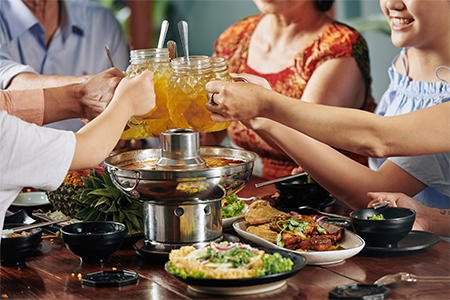 Hands of family members toasting with glass mugs over dinner table with hotpot