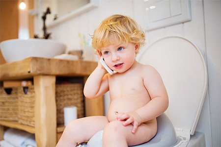 Cute toddler with a smartphone in the bathroom. Little boy sitting on the toilet