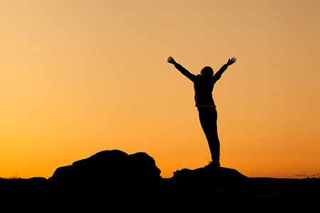 Stock Photo - Silhouette of happy young woman with arms raised up against beautiful colorful sky. Su