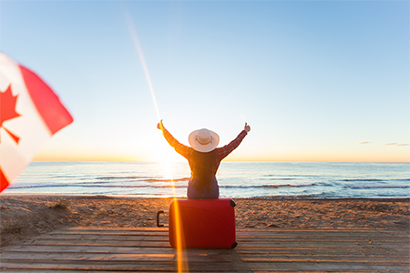 concept - woman tourist sitting near the sea on the red suitcase and in hat and watching sunset and 