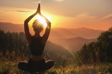 Woman practicing yoga in mountains at sunrise, back view