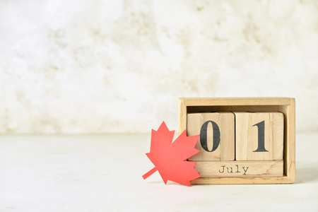 Wooden cube calendar with date JULY 1 and maple leaf on light background