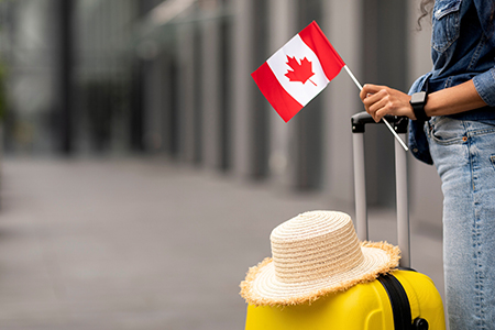 Cropped of woman traveller holding flag of Canada, going abroad