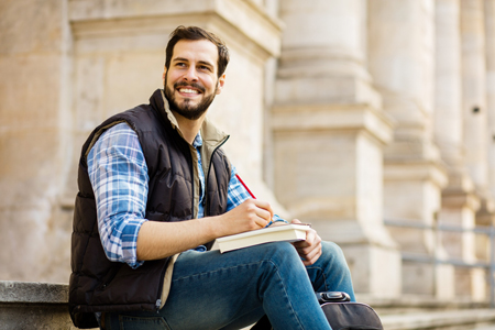 a student sitting on university stairs outside writing on paper