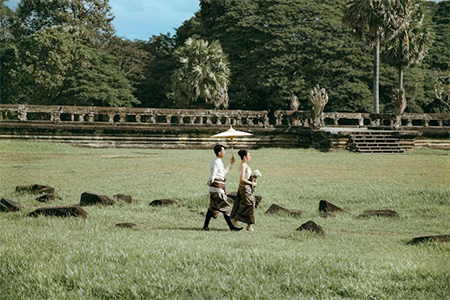 Bride and Groom in Traditional Cambodian Wedding Clothing Walking on a Field