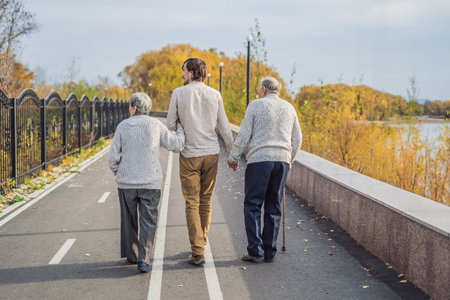 An elderly couple walks in the park with a male assistant or adult grandson. Caring for the elderly,