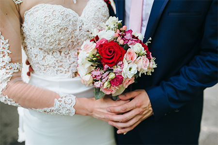 A couple holding bouquet of flowers in wedding dress