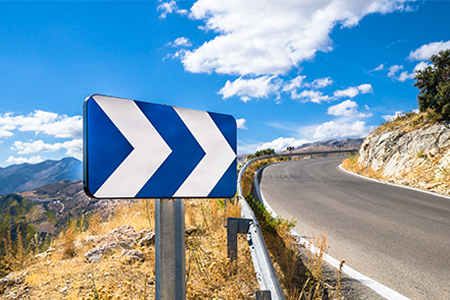 A blue white street sign showing directions next to a road with a scenic background