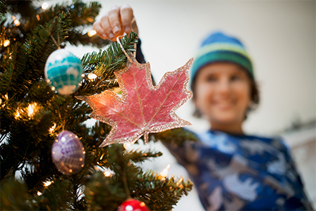 A young boy holding Christmas ornaments and placing them on the Christmas tree