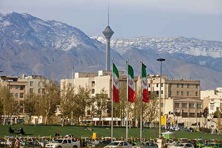 Three waving Iran flags in front of residential buildings, Milad Tower and Alborz Mountains in the c