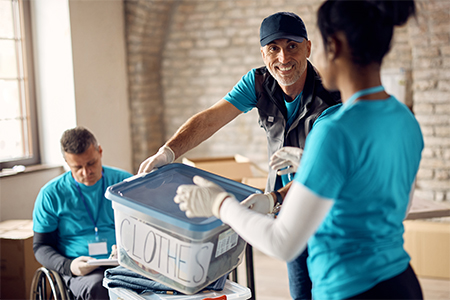 man volunteering at donation center and passing box with clothes to his coworker