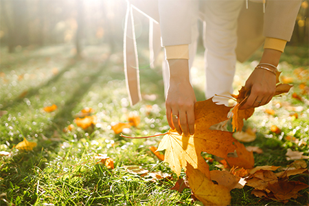 Smiling girl collects yellow leaves in autumn. Young woman enjoying autumn weather