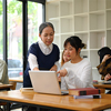 lecturer assisting college student with laptop in classroom