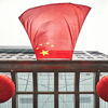 Looking up at Chinese flag and red lanterns on a building.