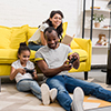 Happy father and daughter playing video games while mother sitting on couch