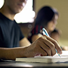 man writing in notebook - woman in background. Selective focus on pen