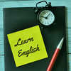 Phrase learn English written on sticky note with a pen,alarm clock and book