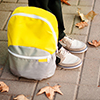 The school boy is ready to go to school. The legs are on the sidewalk, the backpack is near.