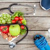 top view of stethoscope, organic vegetables and fruits and sport equipment on wooden surface