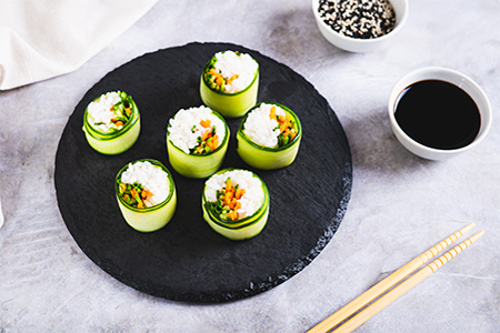 sushi rice, carrots and green onions wrapped in cucumber on a slate board